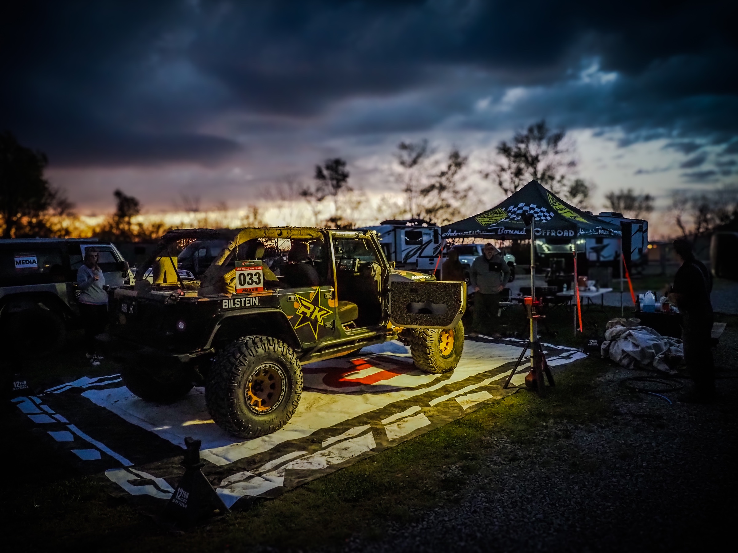 ABO race Jeep at pit camp under a dramatic dusk storm sky